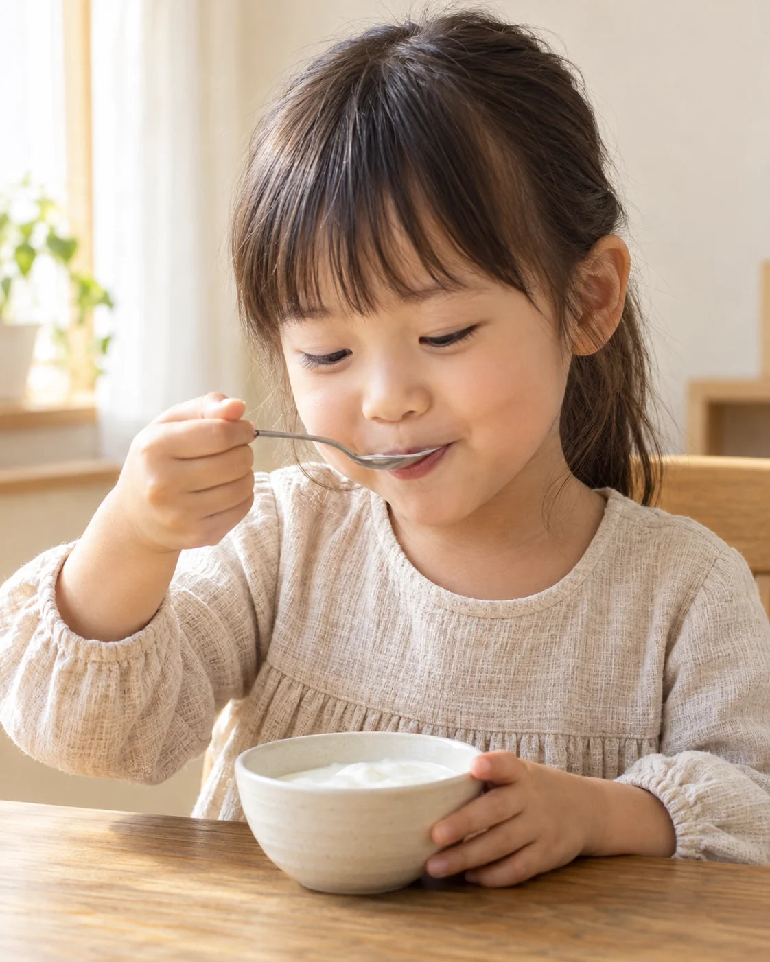 自宅の食卓でヨーグルトをおいしそうに食べる子どもの使用イメージ